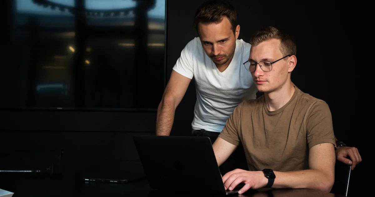 Die zwei jungen Männer Fabian und Sven sitzen in einem dunklem Raum zusammen vor einem Laptop.